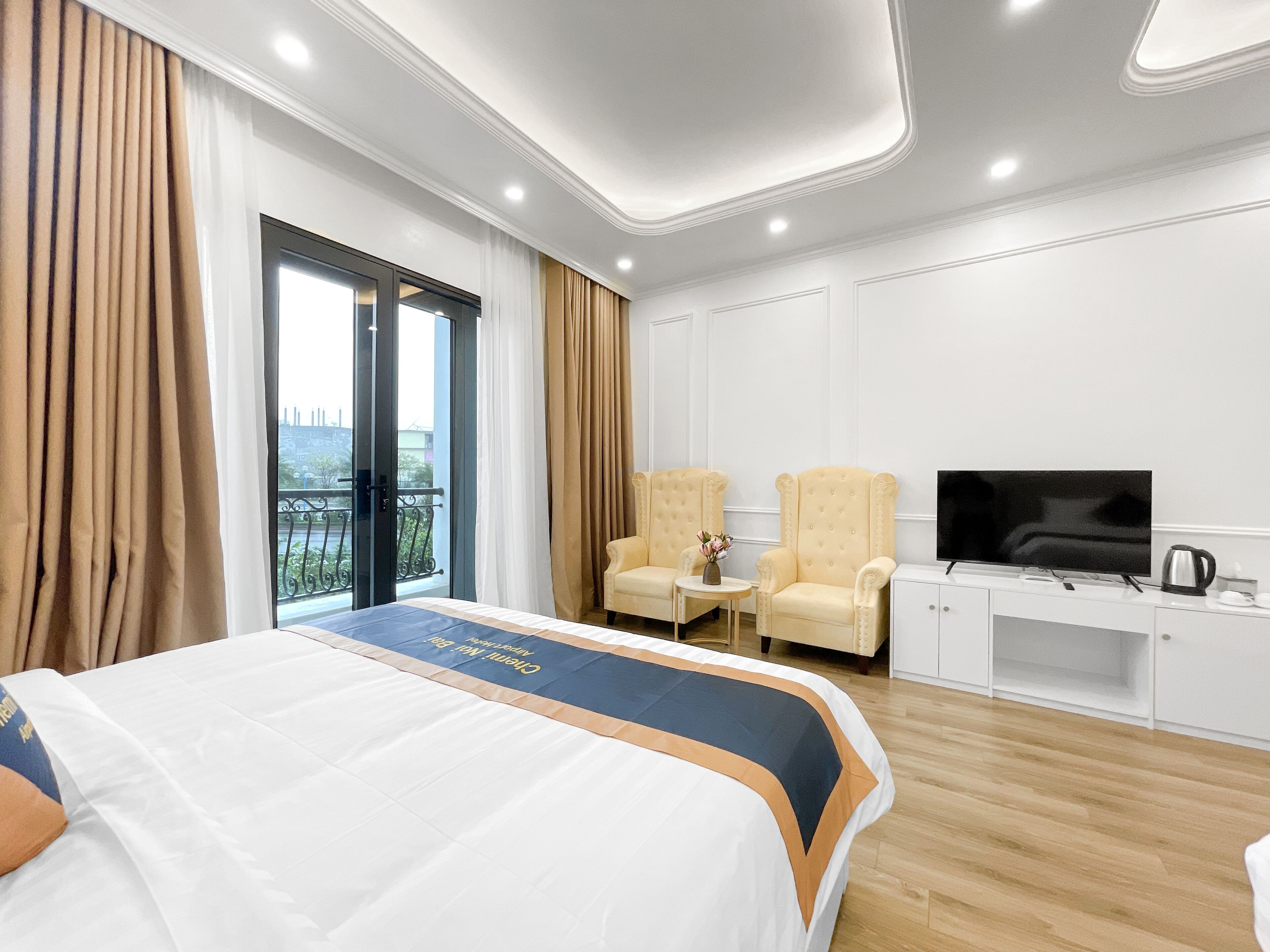 Habitación de hotel con una cama grande, dos sillones, una mesita con un florero, un televisor y un minibar.