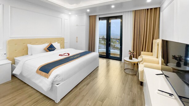 Una habitación de hotel moderna con una cama grande, un sofá, un televisor y un balcón con cortinas.