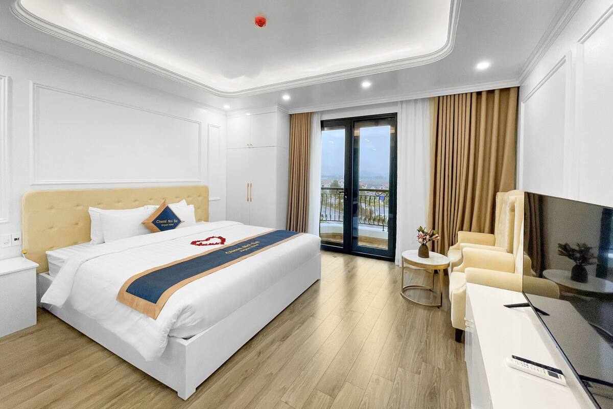 Una habitación de hotel moderna con una cama grande, un sofá, un televisor y un balcón con cortinas.