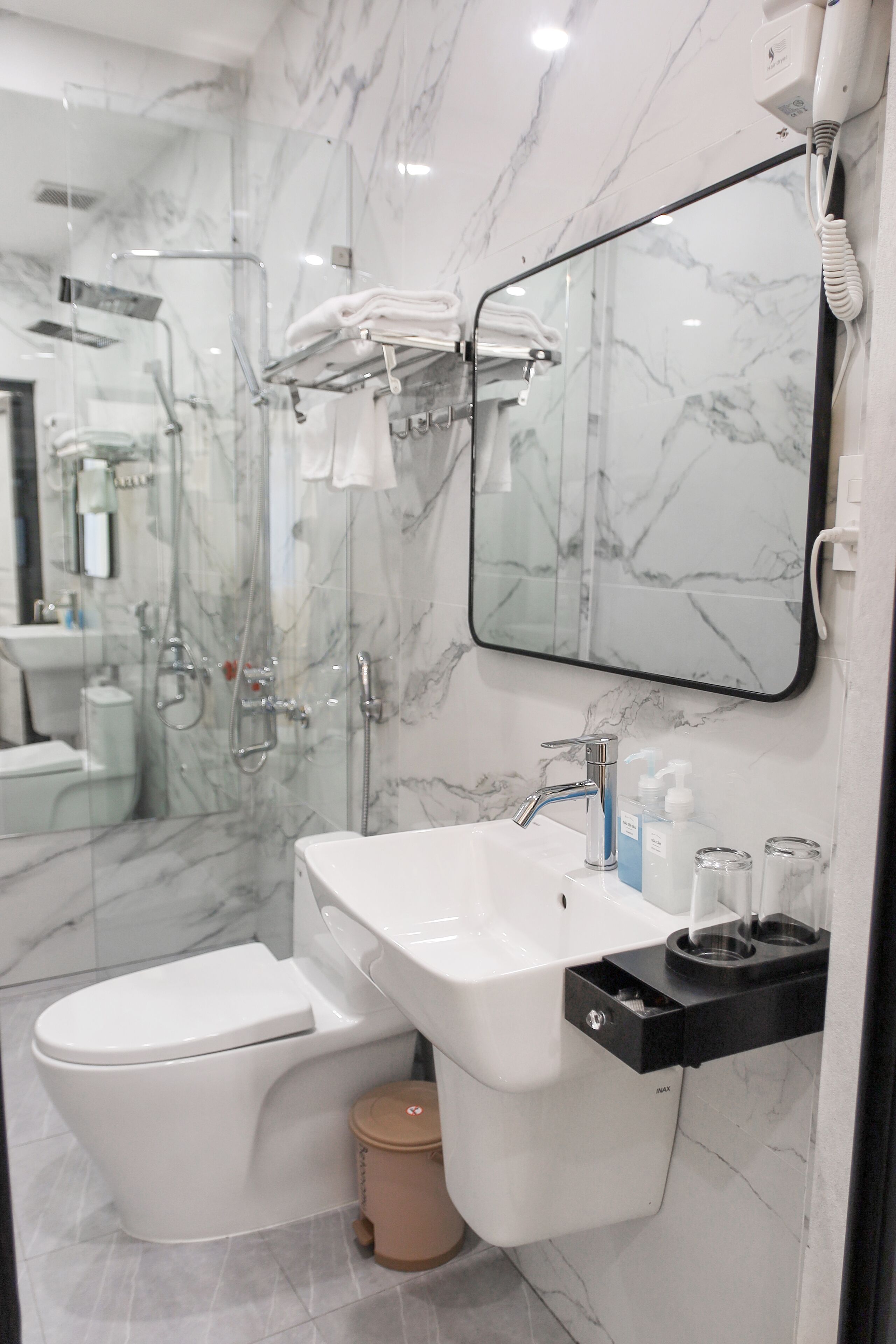 A modern bathroom with a glass-enclosed shower, a white sink, a toilet, and a marble backsplash.
