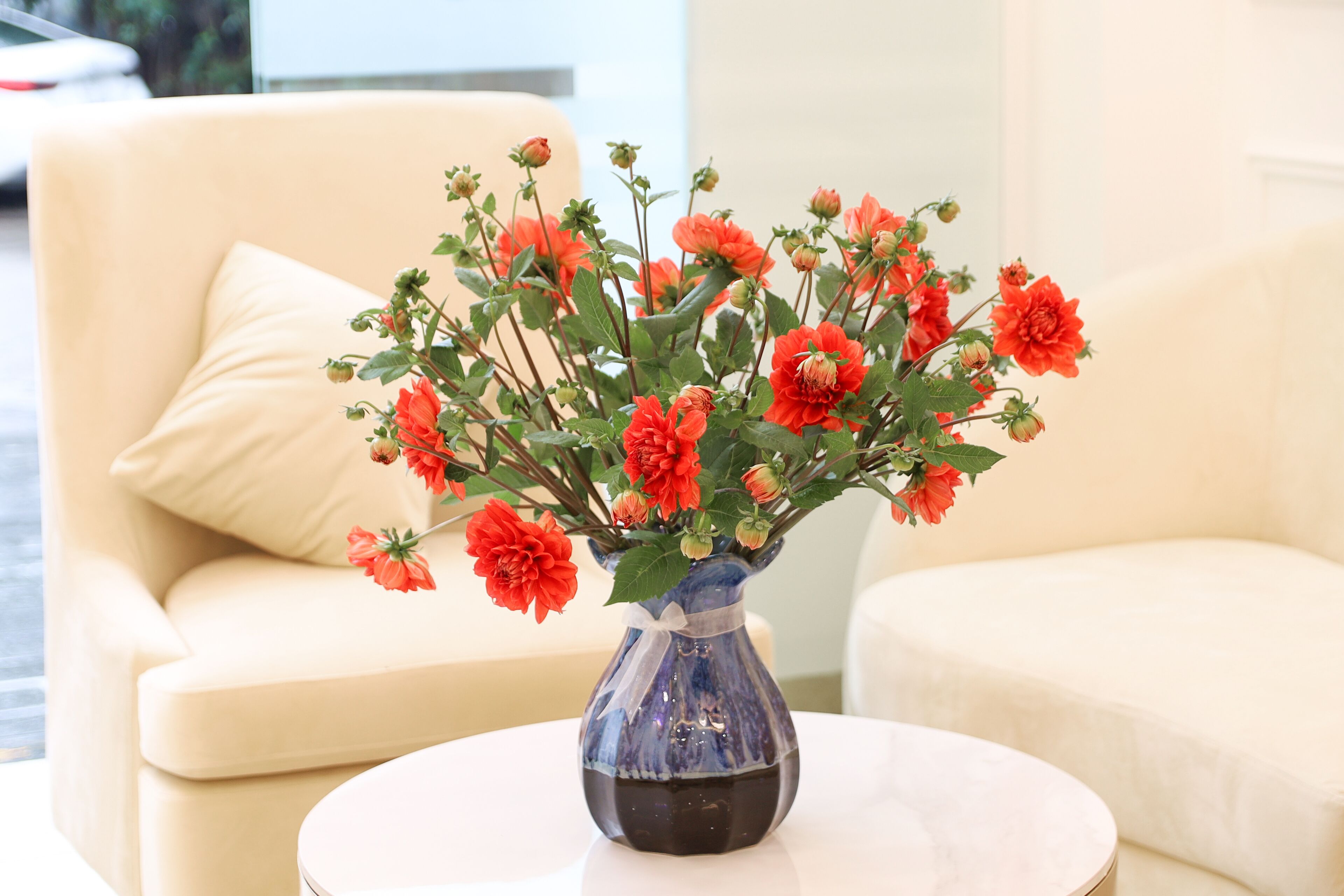 A vase with red flowers on a white table in a room with beige sofas.