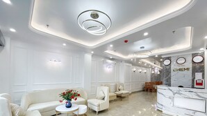 Un moderno vestíbulo de hotel con mostrador de recepción, zona de estar y un jarrón decorativo con flores.
