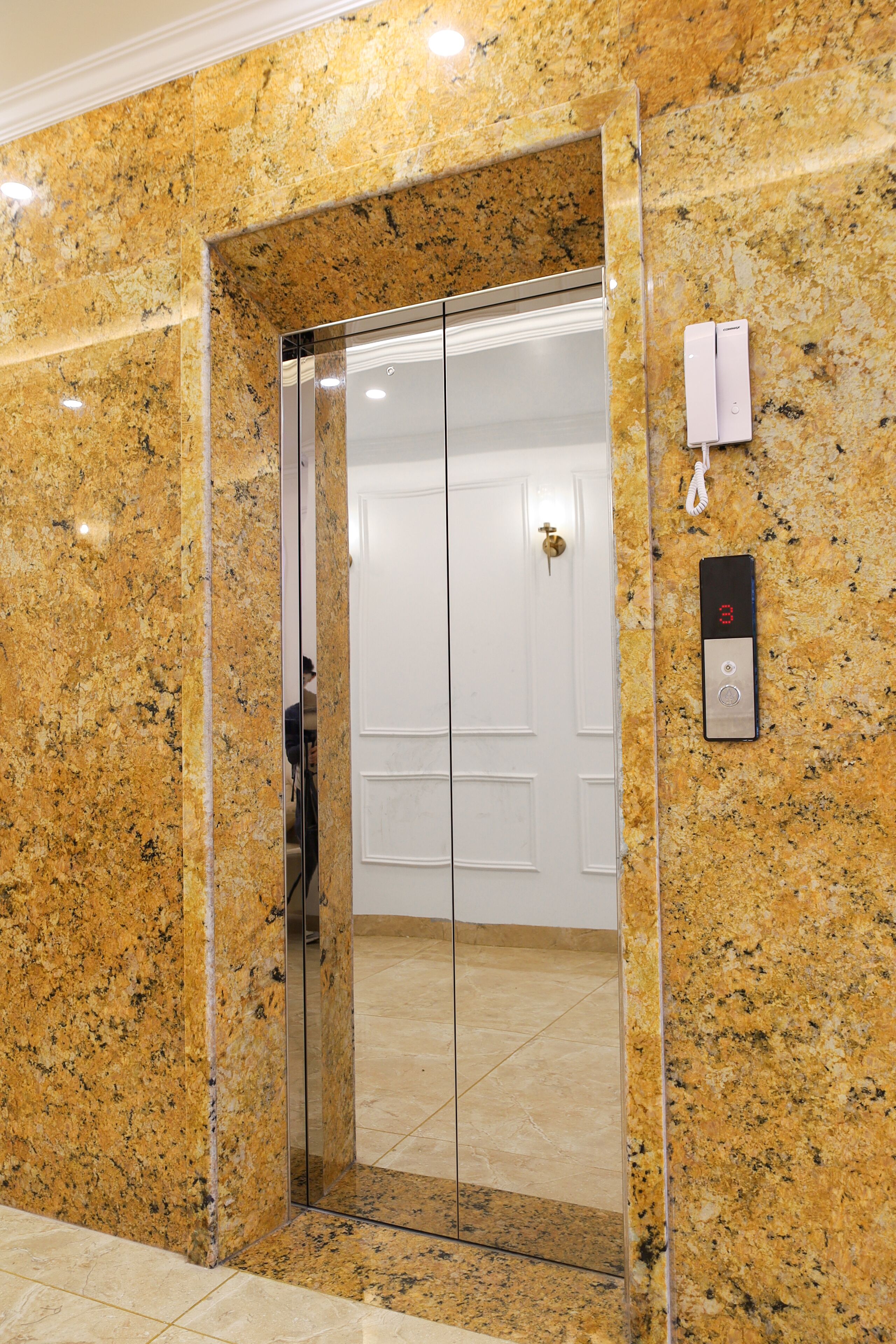A modern elevator with a digital display, a clear glass door, and a marble wall.
