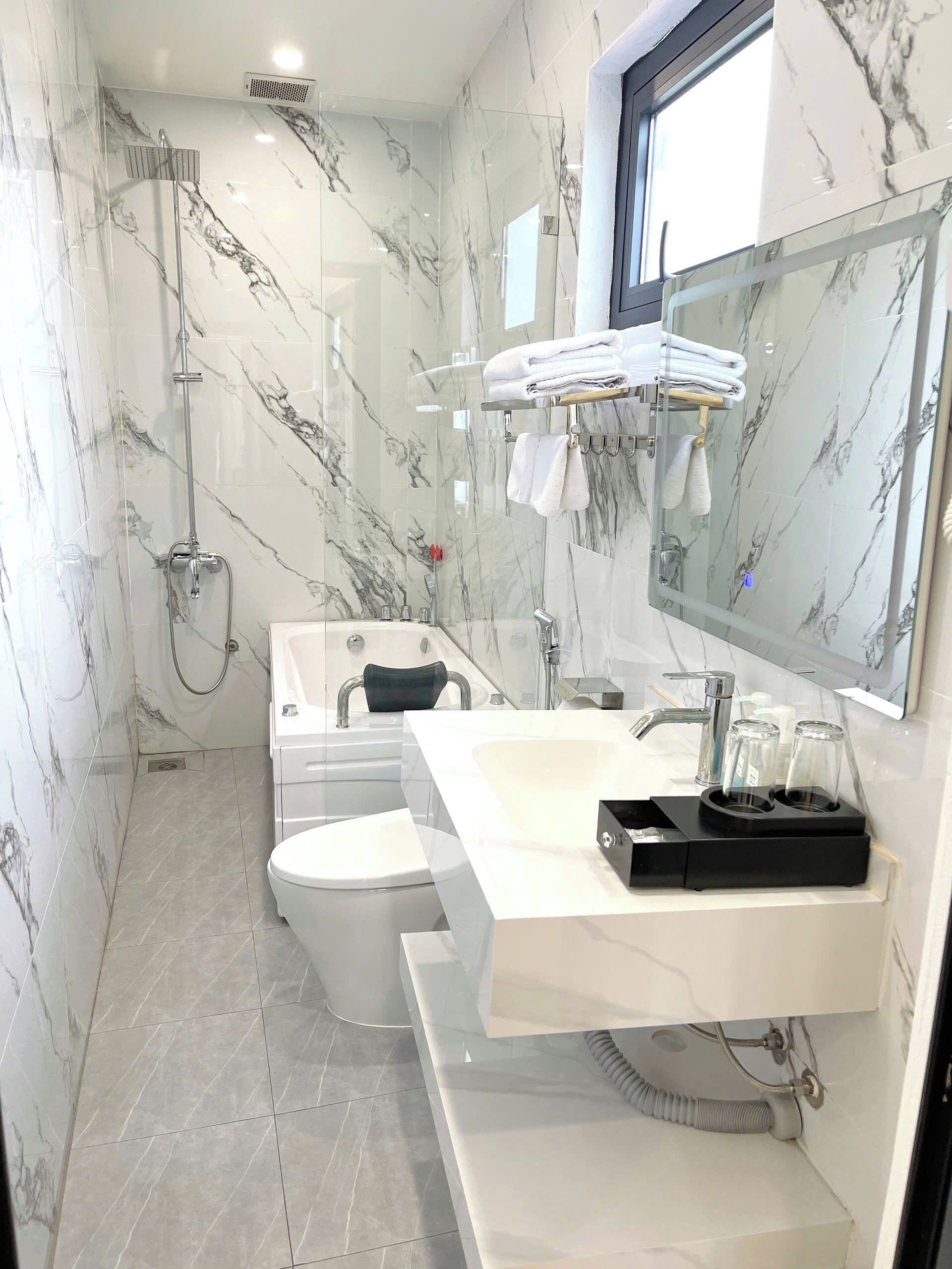 A modern bathroom with a glass-enclosed shower, a white toilet, a sink with a black soap dish, and a large mirror.