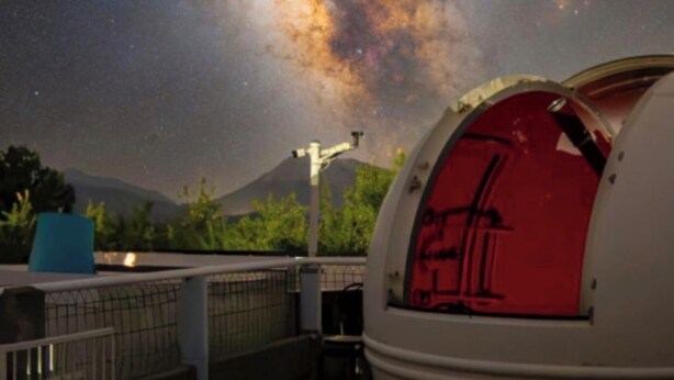Un observatorio abovedado de interior rojo, con un cielo estrellado y una montaña de fondo.