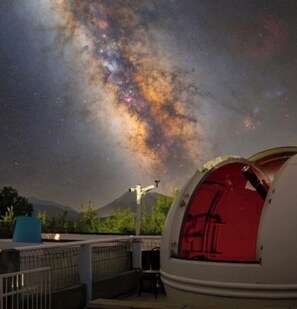A dome-shaped observatory with a red interior, set against a backdrop of a starry night sky and a mountain.