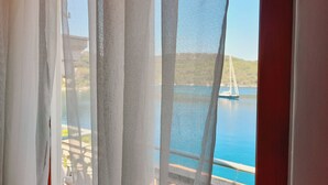 A view through sheer curtains of a sailboat on a calm body of water, with a hilly landscape in the background. - Apartments Sponga (Mljet)
