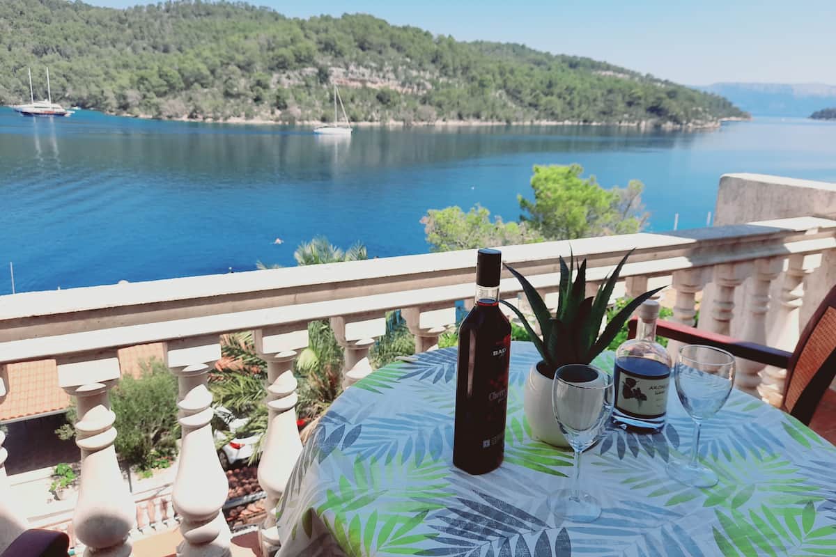 A balcony with a table set for two, overlooking a body of water and a forested hill.