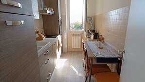 Een smalle keuken met houten keukenkastjes, een eettafel met stoelen en een raam dat voor natuurlijk licht zorgt.