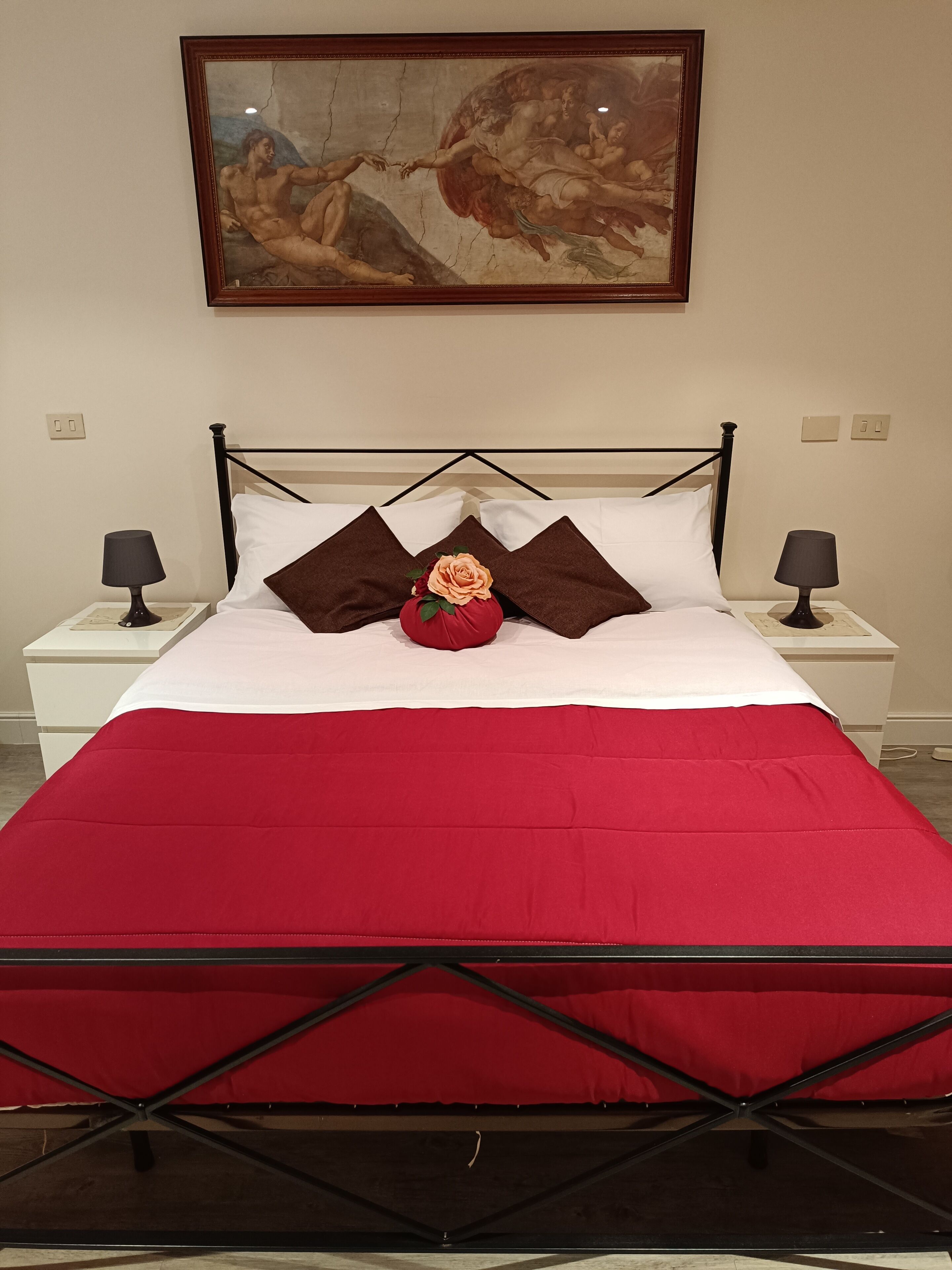 Ein Bett mit roter Bettdecke, zwei braunen Kissen und einer Rosenarragemement.