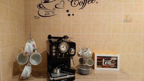 Een koffieapparaat, mokken en een theebox op een plank tegen een betegelde muur met een bord waarop 'Coffee' staat.