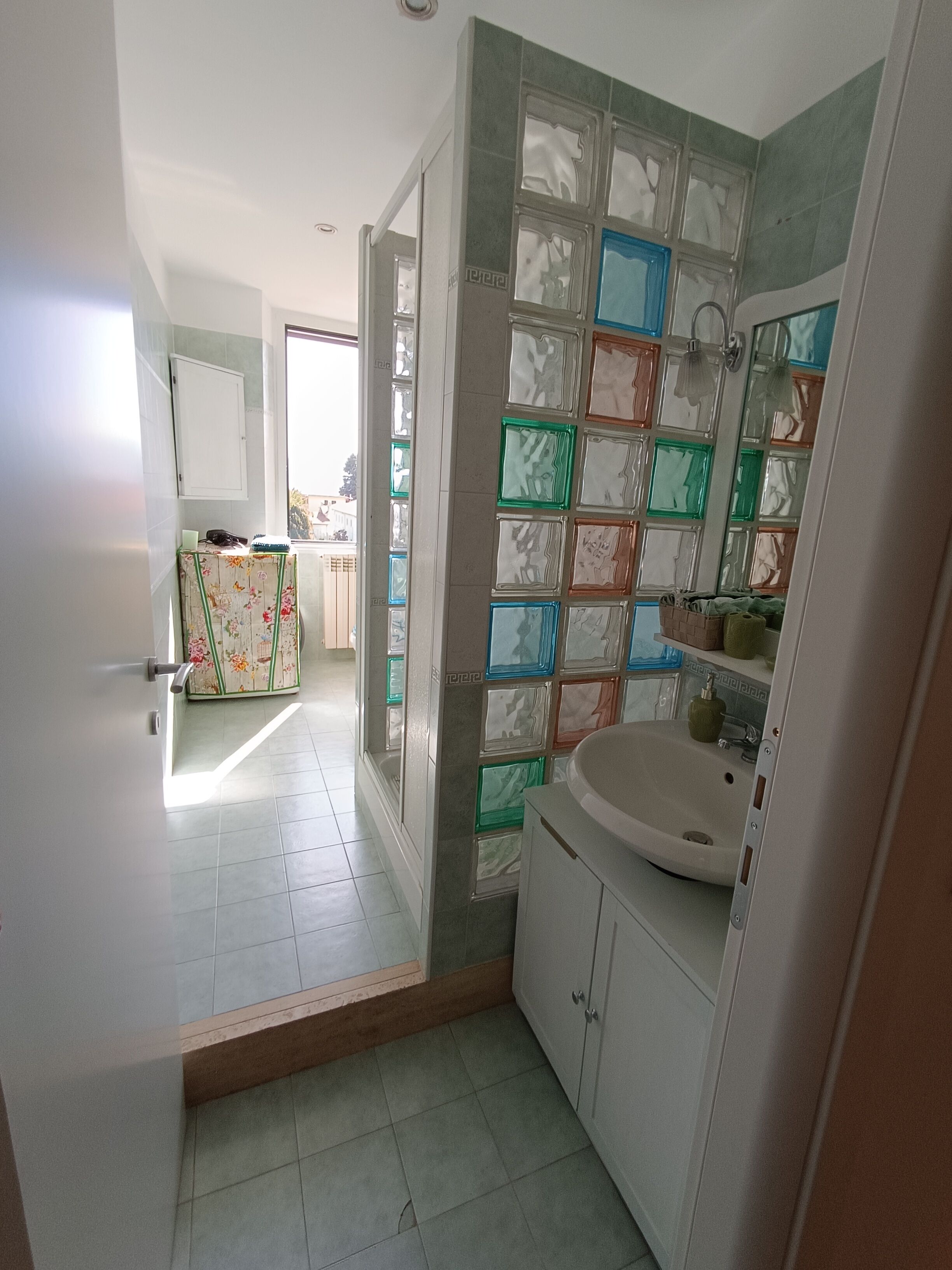 A bathroom with a sink, mirror, and tiled walls. There is a door leading to another room.