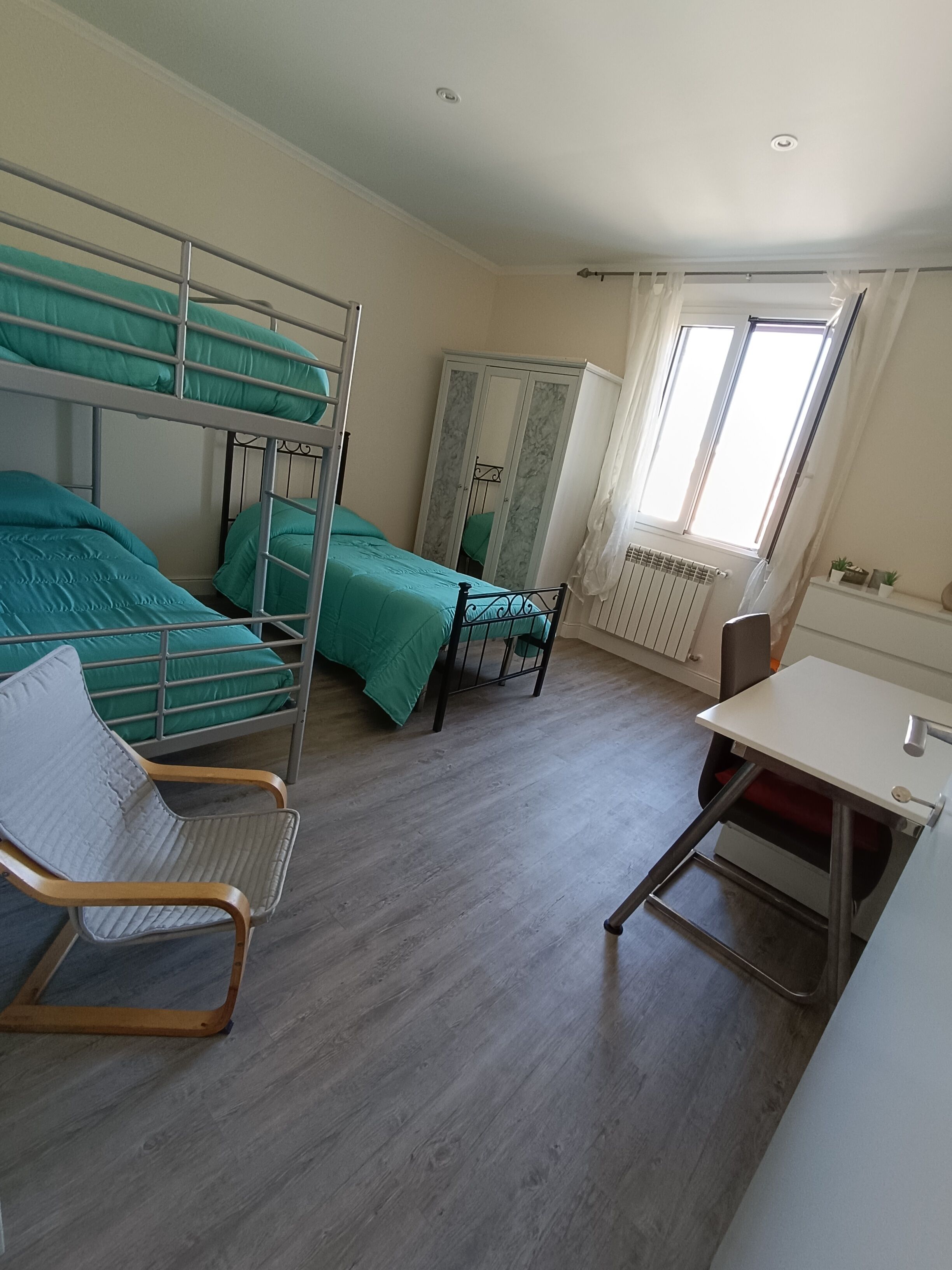 A dormitory room with bunk beds, a desk, a chair, a wardrobe, and a radiator.