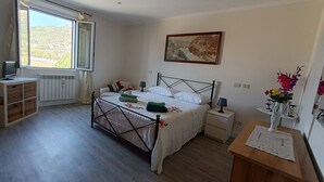 Een slaapkamer met een bed, nachtkastjes, een dressoir, een radiator, een raam met uitzicht en een schilderij aan de muur.