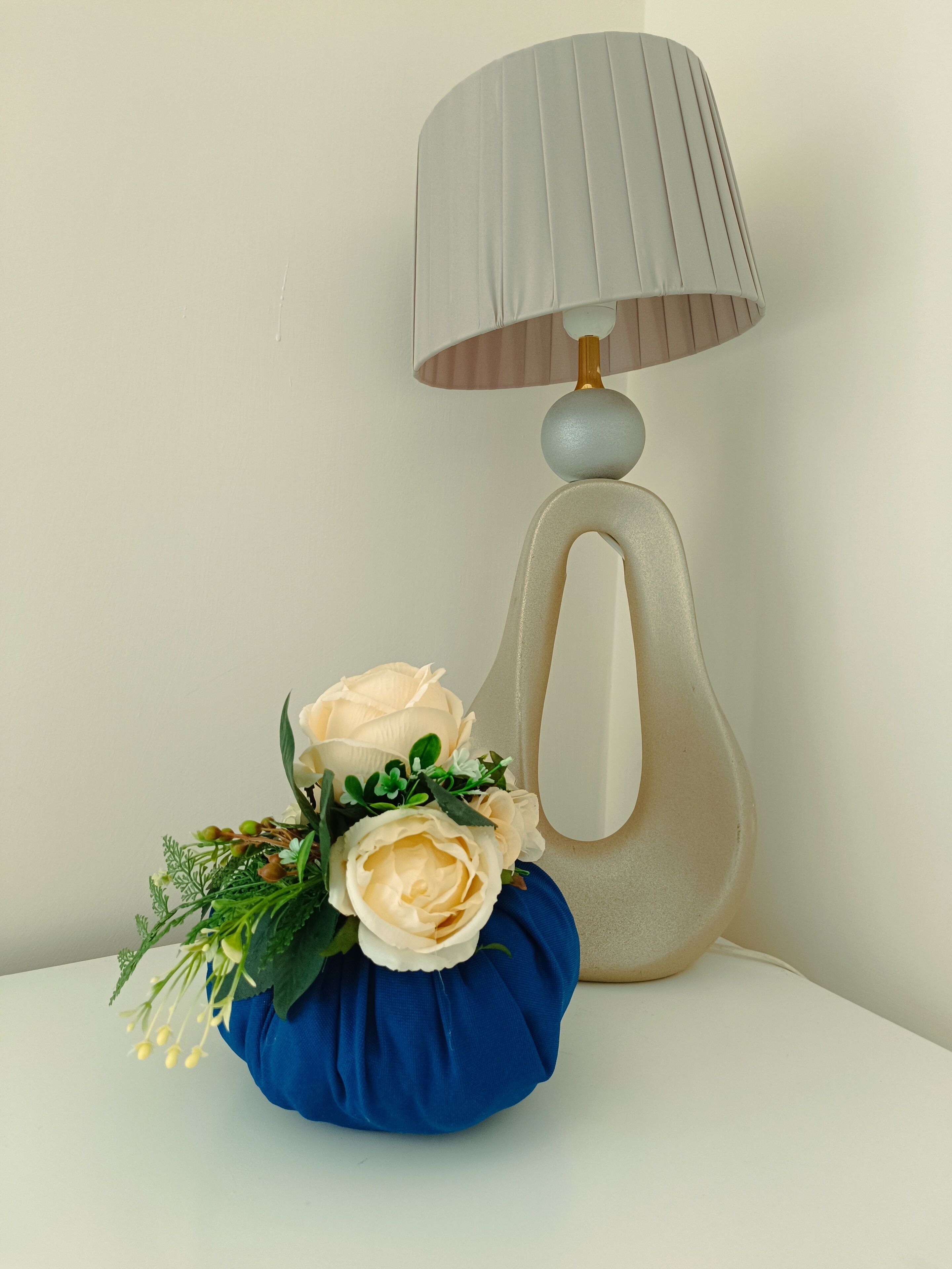 Una lampada con un paralume beige e un cuscino blu decorato con rose bianche e verde.