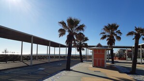 A covered walkway with palm trees, a small red kiosk, and a view of the beach. - Beautiful AC T2 for 4, terrace and parking in Port Leucate (Port Leucate)