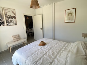 Une chambre à coucher avec un lit, un banc, une porte et un mur orné d’un tableau.