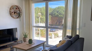A living room with a sofa, a TV, a table with a plant, and a view of a garden through large windows. - Beautiful AC T2 for 4, terrace and parking in Port Leucate (Port Leucate)