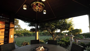 An outdoor patio with a round table, chairs, a fire pit, and a decorative stained glass light fixture.