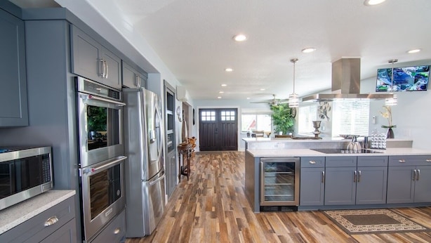 A modern kitchen with stainless steel appliances, grey cabinetry, and a wooden floor.