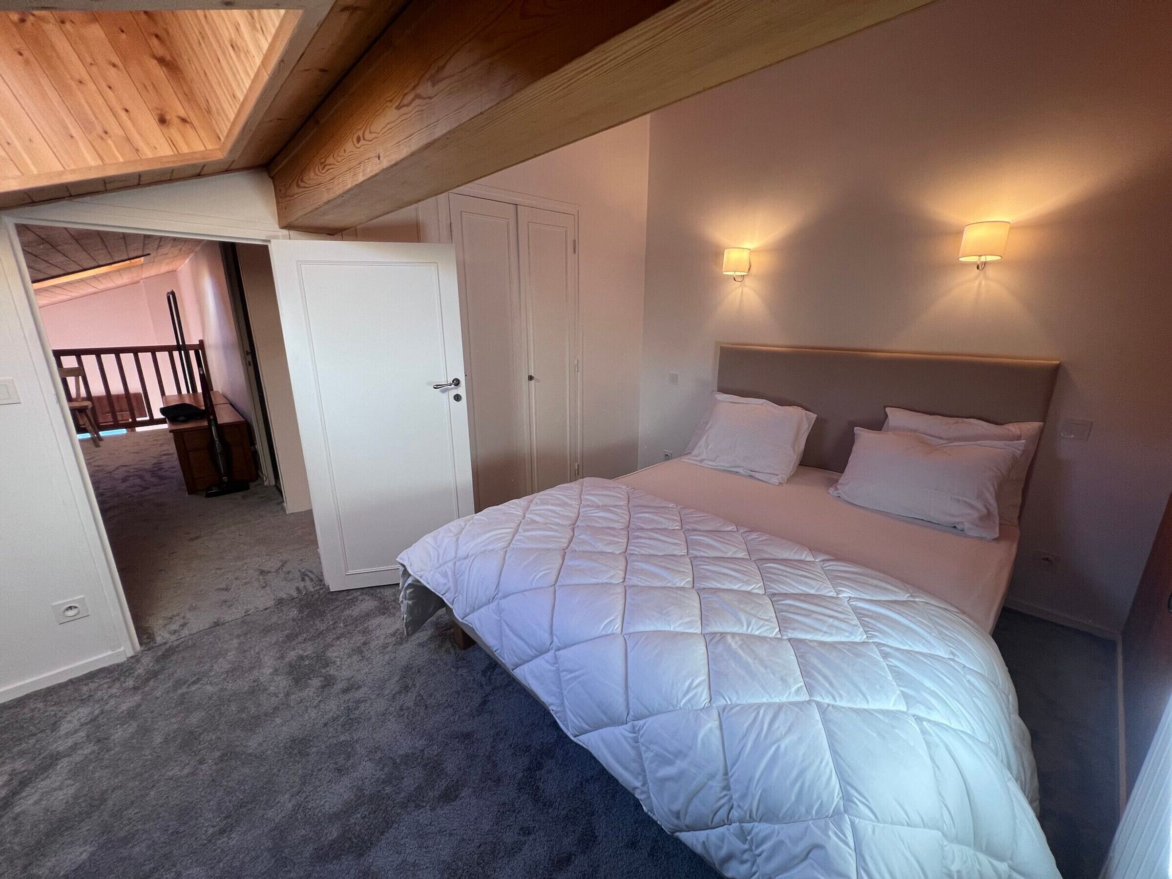 A bedroom with a large bed, two bedside lamps, and a door leading to another room.