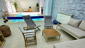 A poolside area with lounge chairs, a sofa, and a small table. - Maison Bourgogne 400m2, 2 Piscines Intérieure/extérieure,spa, Commerces à 50m (Gueugnon)