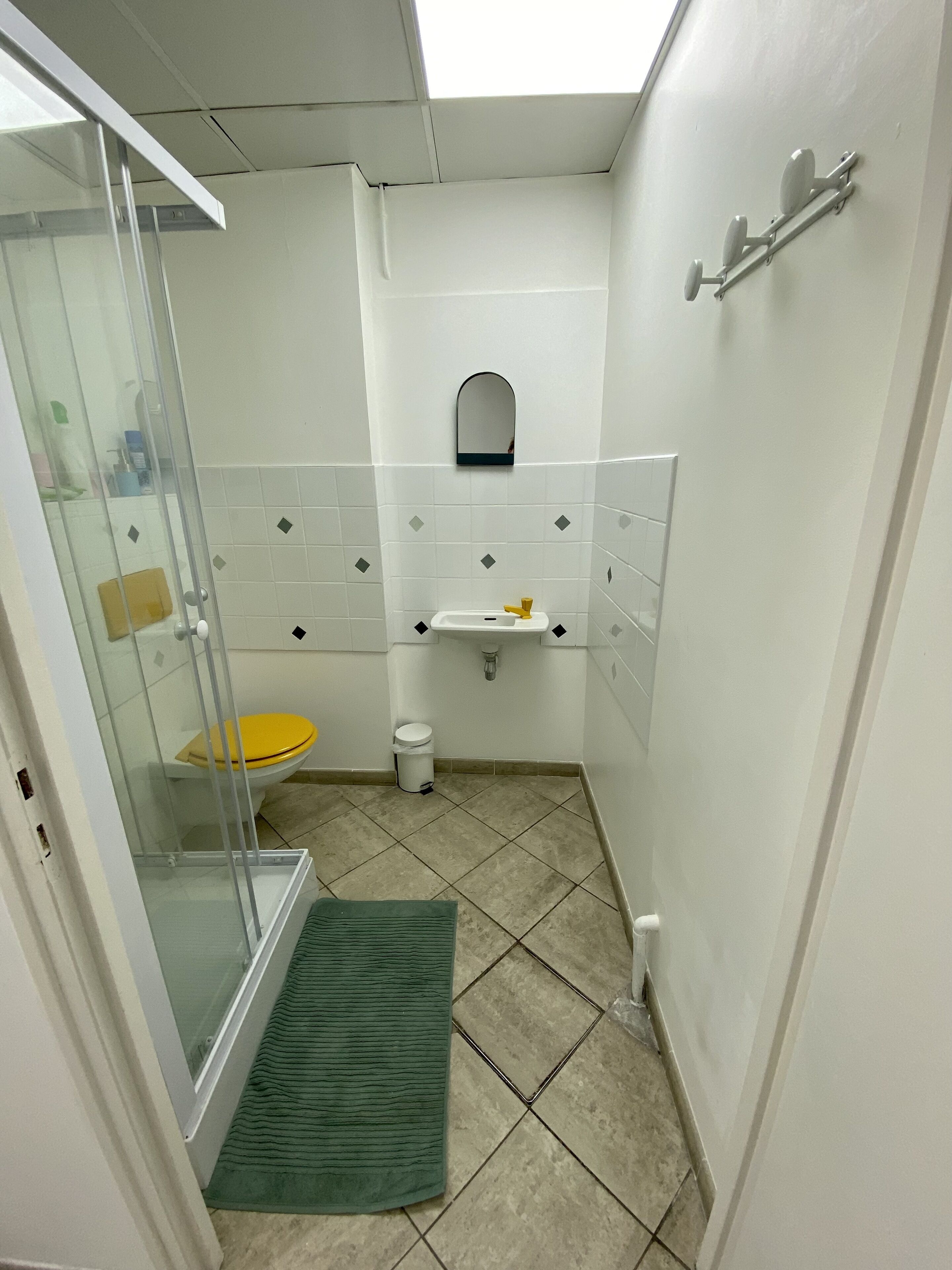 A small, compact bathroom with a glass shower enclosure, a yellow toilet, and a white sink with a mirror above it.
