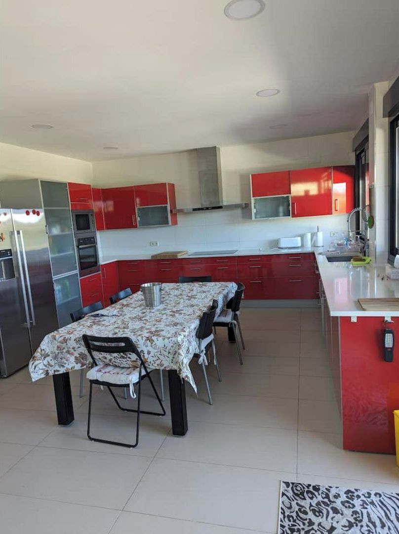 A modern kitchen with red cabinets, a dining table with chairs, and stainless steel appliances.