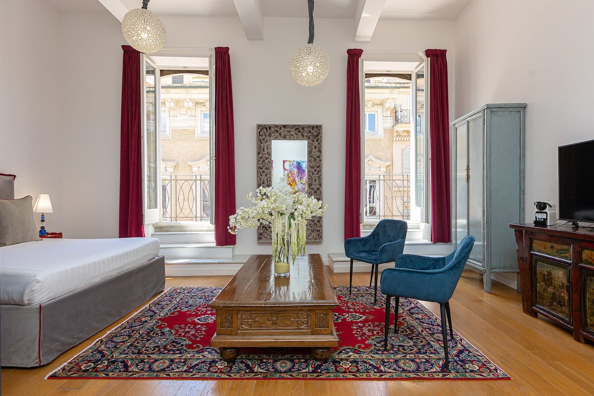A bedroom with a bed, a coffee table with a vase of flowers, a blue chair, and a TV on a cabinet.