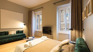 A hotel room with a bed, a green sofa, a TV, and a window with curtains. - SUITE DELLA PIGNA (Rome)