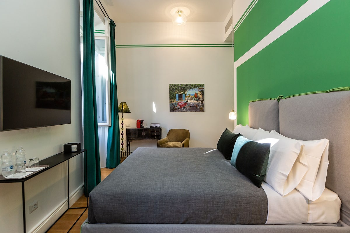 A neatly arranged hotel room with a large bed, a desk with a lamp, a chair, and a TV mounted on the wall.