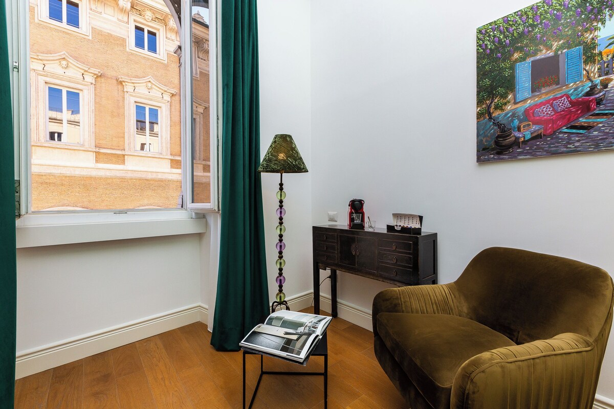 A room with a window, a lamp, a sofa, a small table, and a painting on the wall.