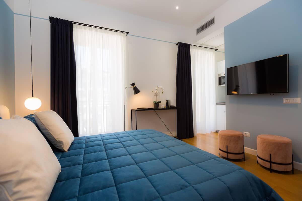 A modern bedroom with a large bed, a TV, and a desk with a lamp.