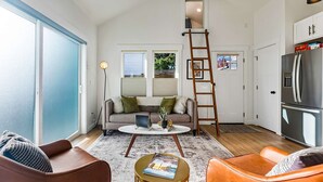 Ein großzügiges Wohnzimmer mit hoher Decke, einer Couch, einem Couchtisch und einer an der Wand stehenden Leiter.