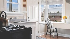 A kitchen with white cabinets, a stove, a sink, and a window with a view of a house. - Walk to the waterfront! The Cozy Cottag (Tacoma)