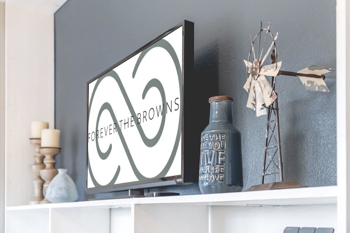A framed artwork with the text "FOREVER THE BROWNS" on a white background, a decorative metal wind chime, and a vase with text on it.