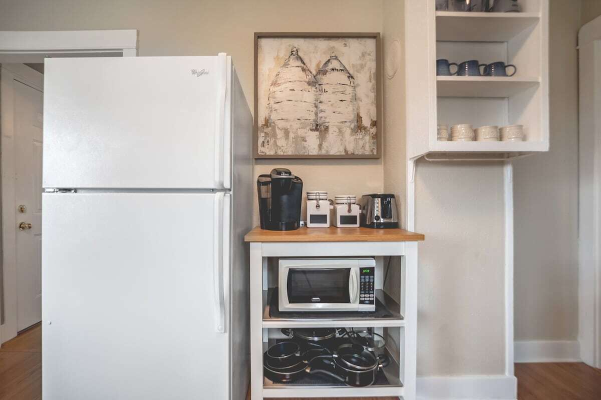 Eine kleine Küche mit einem weißen Kühlschrank, einer Mikrowelle und einer Kaffeemaschine auf einem Holzregal.