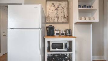 Eine kleine Küche mit einem weißen Kühlschrank, einer Mikrowelle und einer Kaffeemaschine auf einem Holzregal.