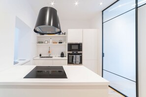 Une cuisine moderne dotée d’un îlot central, d’un four à micro-ondes encastré et d’une grande hotte noire.