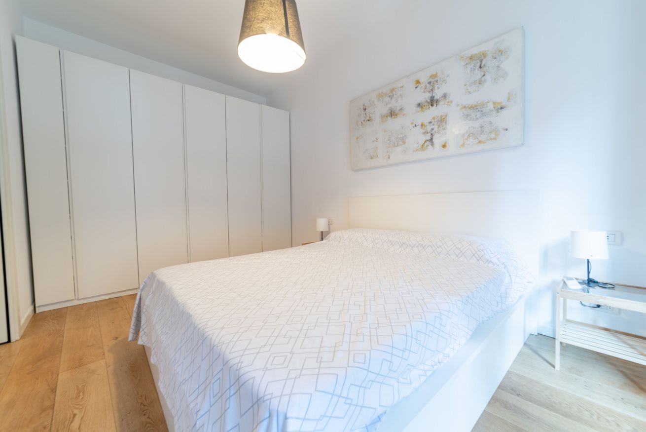 A bedroom with a bed, a wardrobe, a desk, and a wall-mounted abstract art piece.