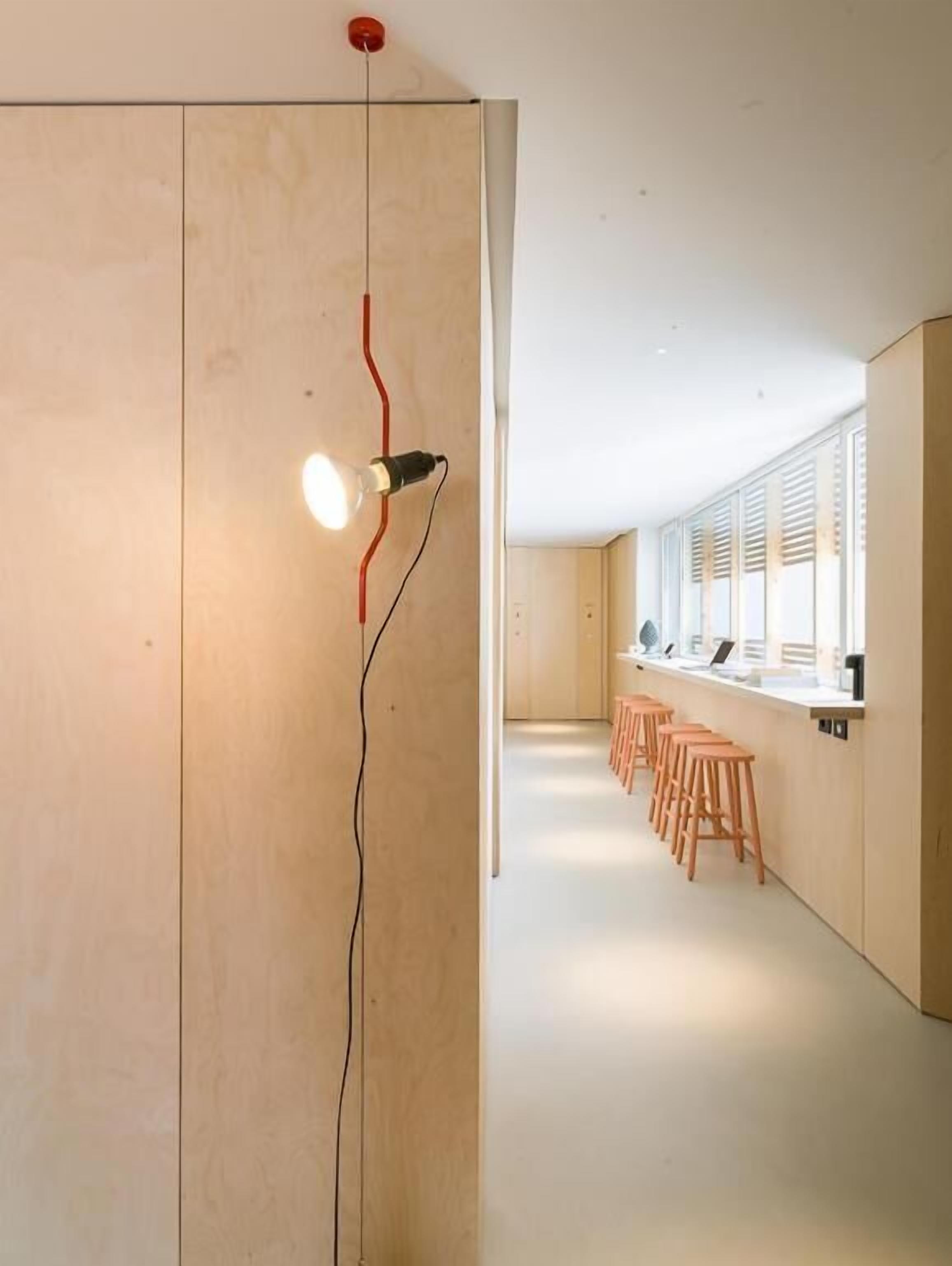 A modern interior with a wooden partition, a hanging light fixture, and a row of wooden stools.