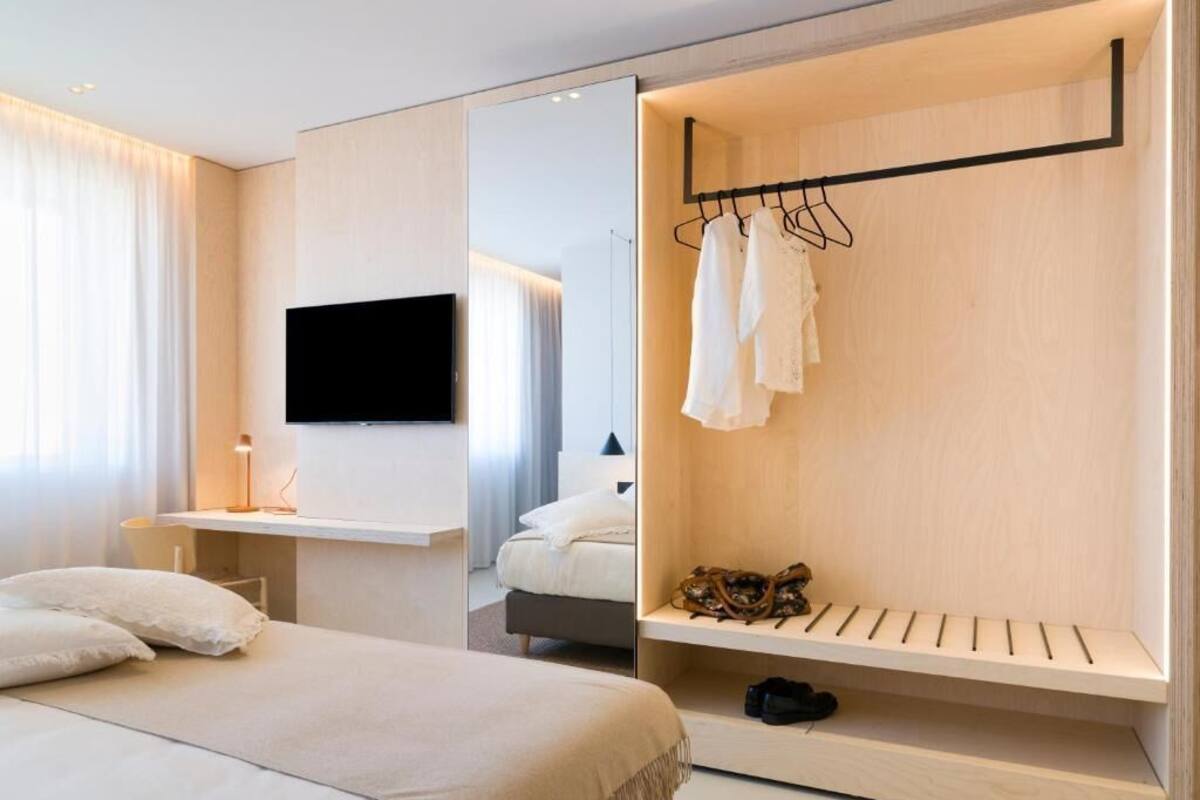 Een moderne hotelkamer met een bed, een aan de muur bevestigde televisie, een houten garderobe met hangende kleding en een schoenenrek.