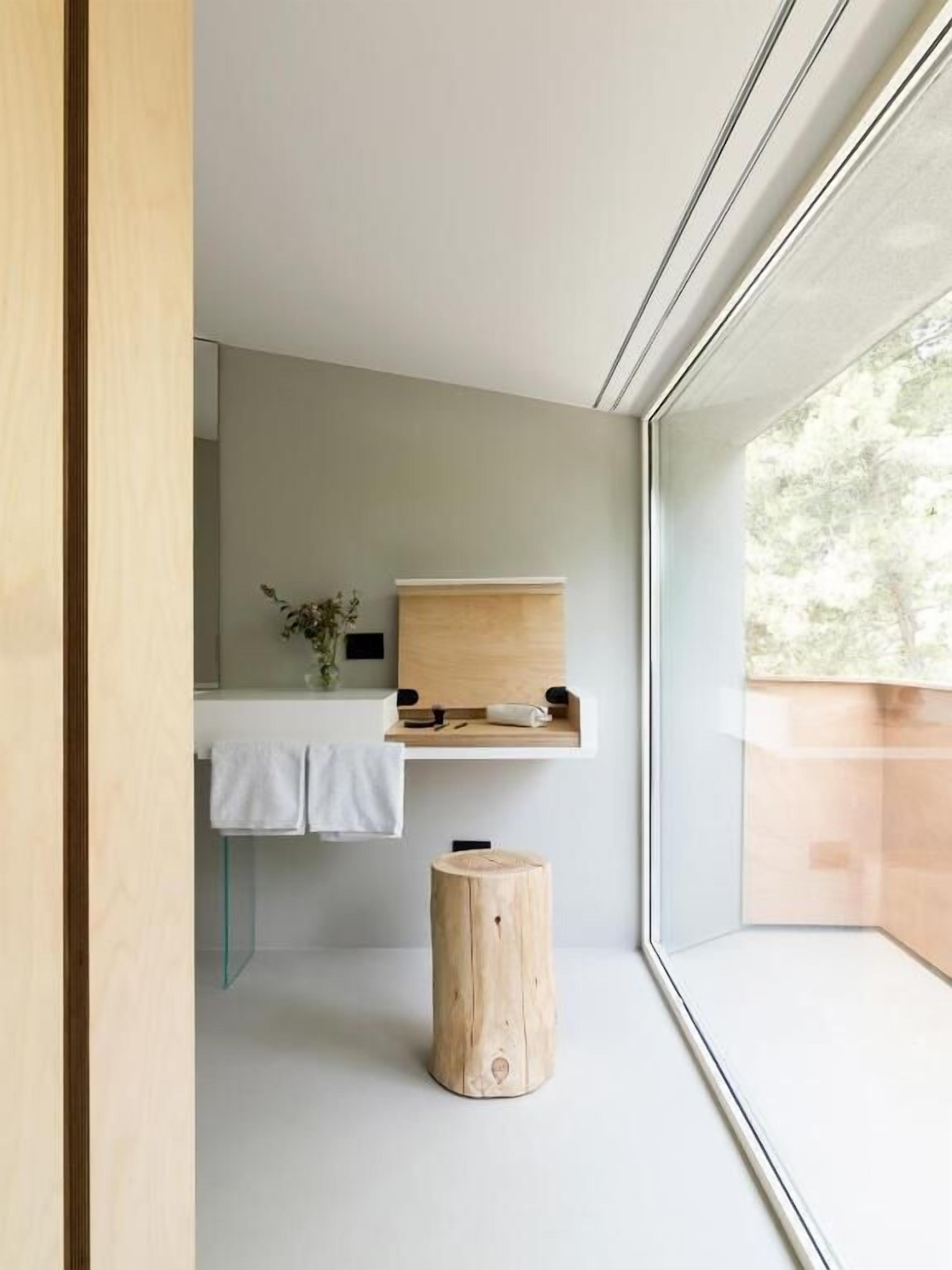 A modern bathroom with a wooden vanity, a small stool, and a glass shower enclosure.