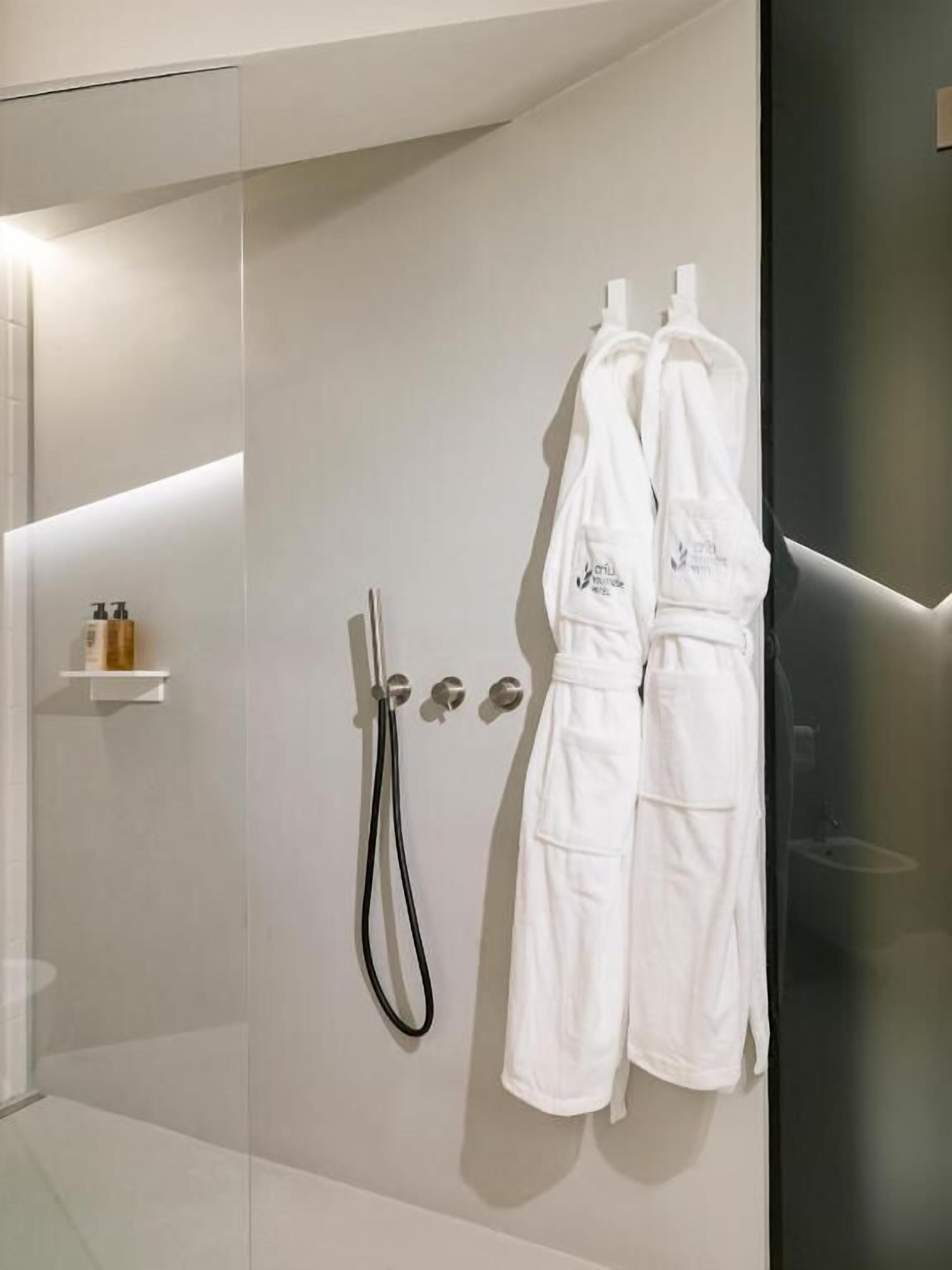 Une salle de bain moderne avec une douche à parois de verre, des peignoirs blancs accrochés au mur et une petite étagère contenant des articles de toilette.