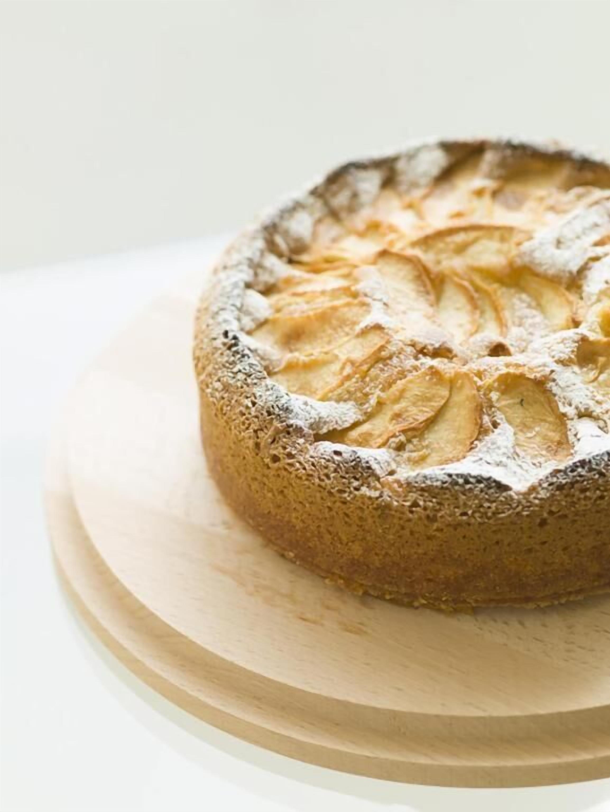 Un gâteau rond, saupoudré de sucre glace sur le dessus, posé sur une planche en bois.