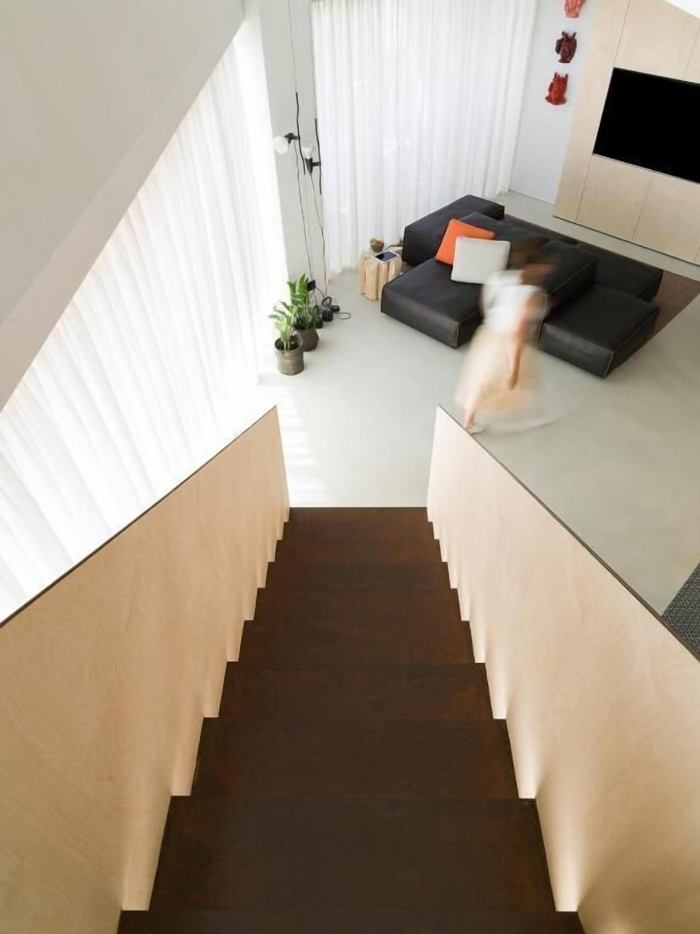Ein modernes Wohnzimmer mit einer Couch, einem an der Wand montierten Fernseher und einer Treppe, die zu einer oberen Etage führt.
