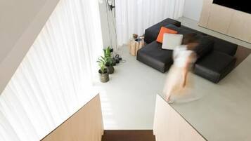 Ein modernes Wohnzimmer mit einer Couch, einem an der Wand montierten Fernseher und einer Treppe, die zu einer oberen Etage führt.
