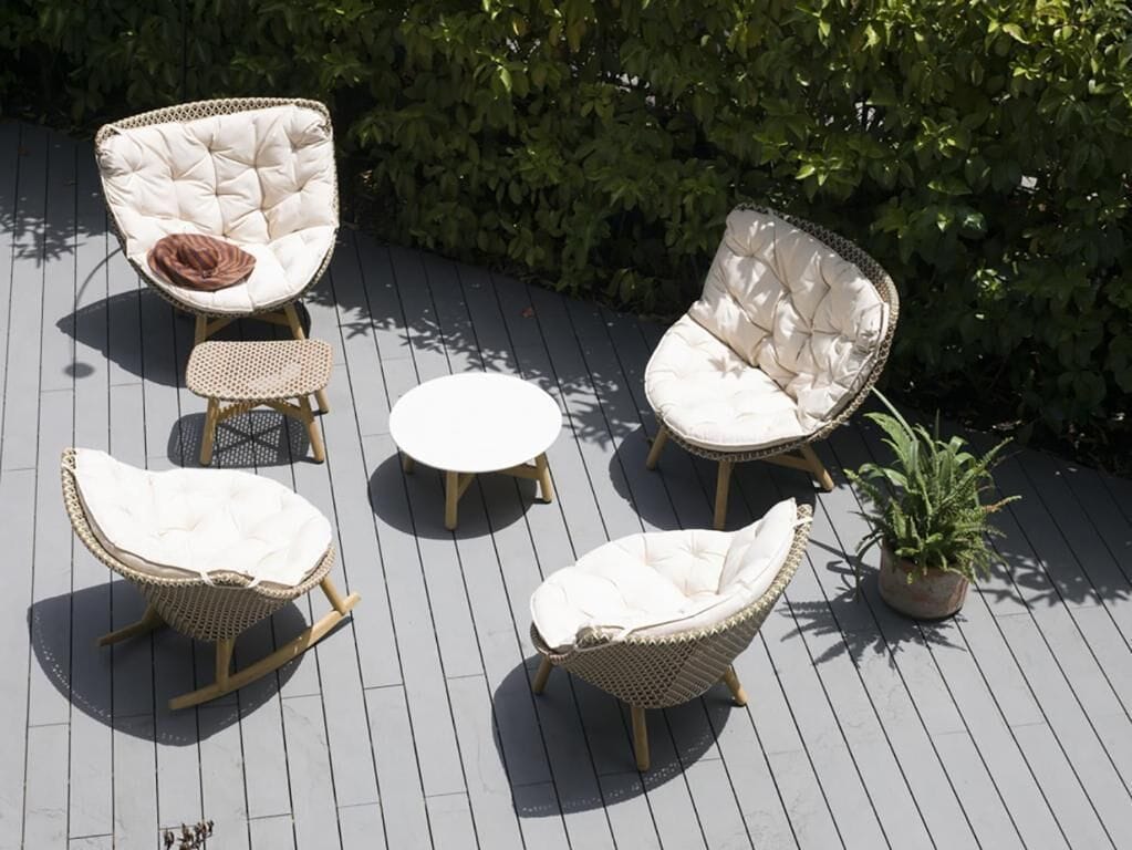 A deck with wicker furniture including two chairs and a small table, surrounded by greenery.