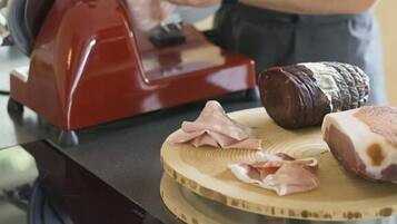 Une personne utilise une trancheuse à viande sur une planche à découper, à côté de morceaux de viande crue et d’une tranche de viande déjà coupée.