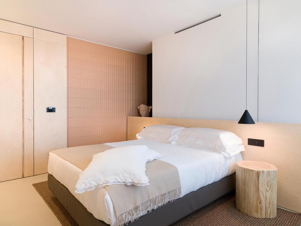 Een moderne slaapkamer met een bed, nachtkastje en een houten wandpaneel.